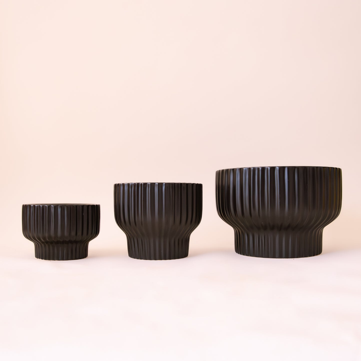 Three different sizes of the black ribbed pedestal planter.