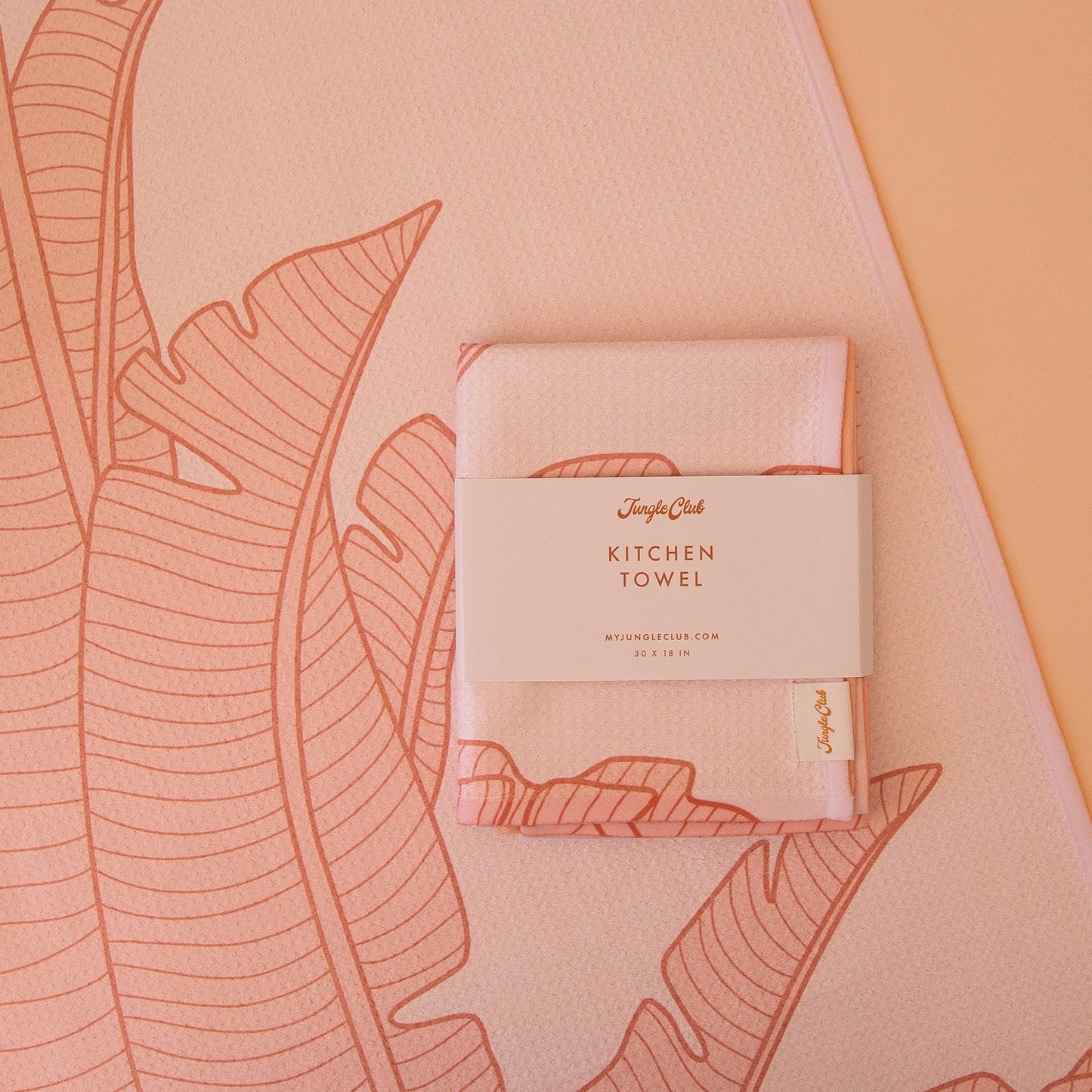 On an orange background is a salmon pink kitchen towel with a bird of paradise pattern.