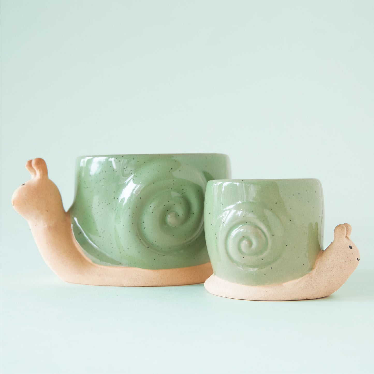 Two ceramic planters in the shape of a snail with smiling faces and a swirly green "shell".