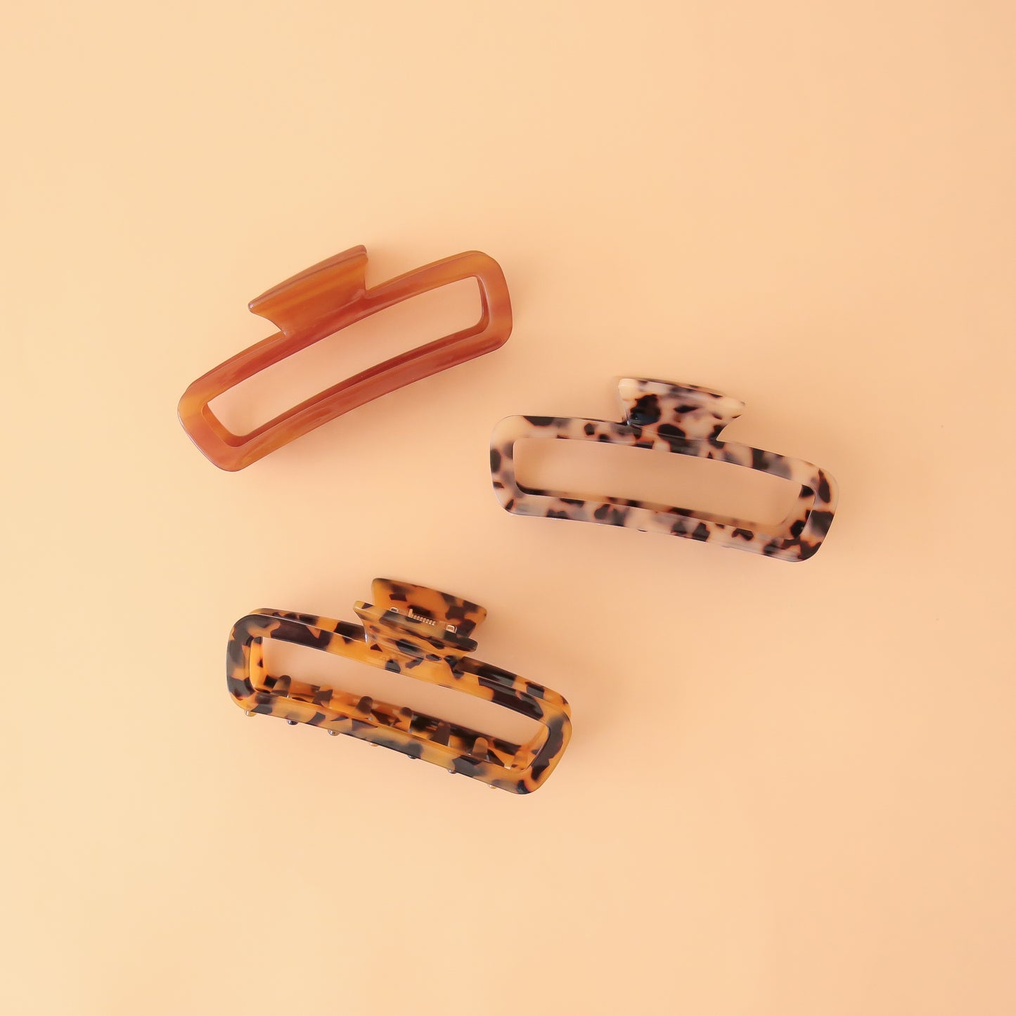 On a light peachy background is three of the Cabana Hair Claws in the shade, honey, light tortoise and tortoise.