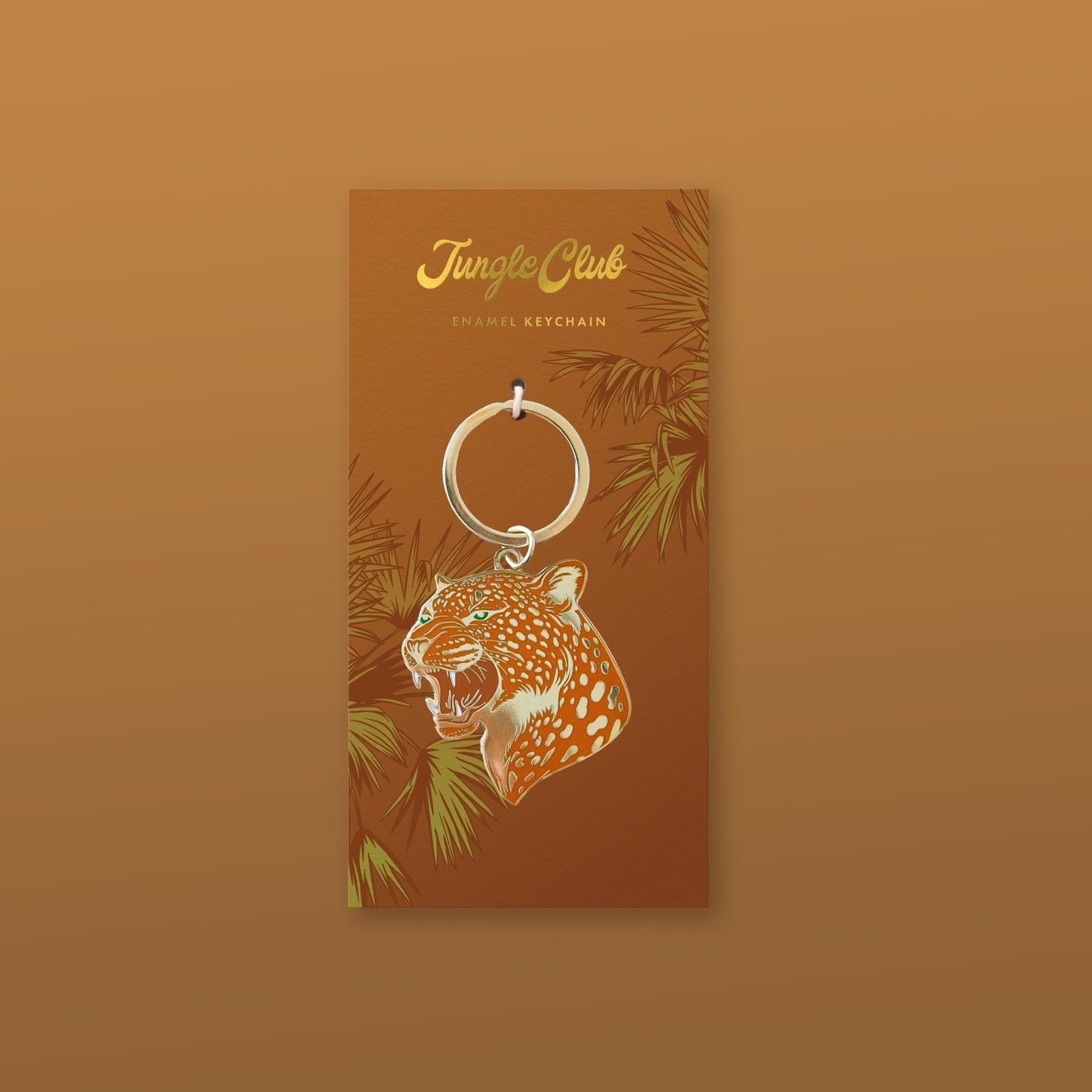 An orange leopard print enamel keychain on a keychain backer with leaf pattern.