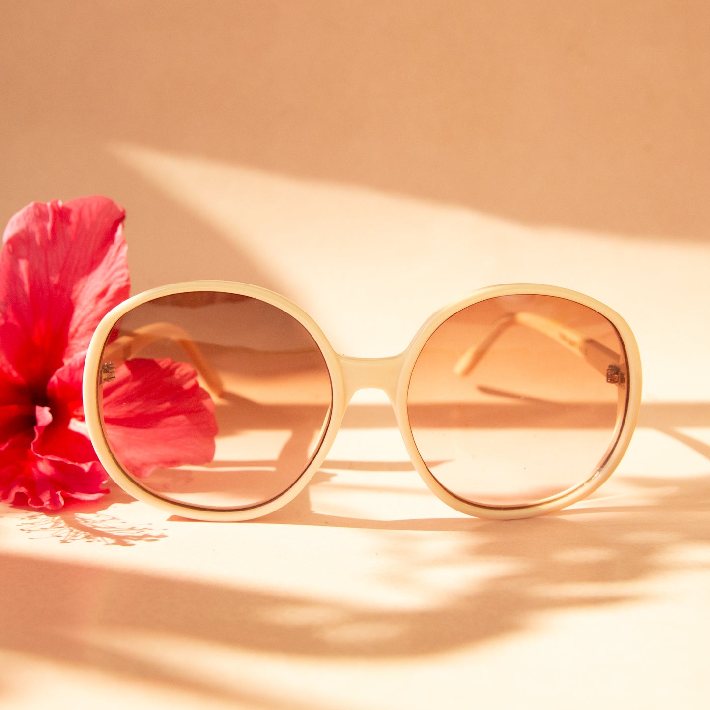 A creamy white pair of round oversized sunglasses with a light brown / pink lens.