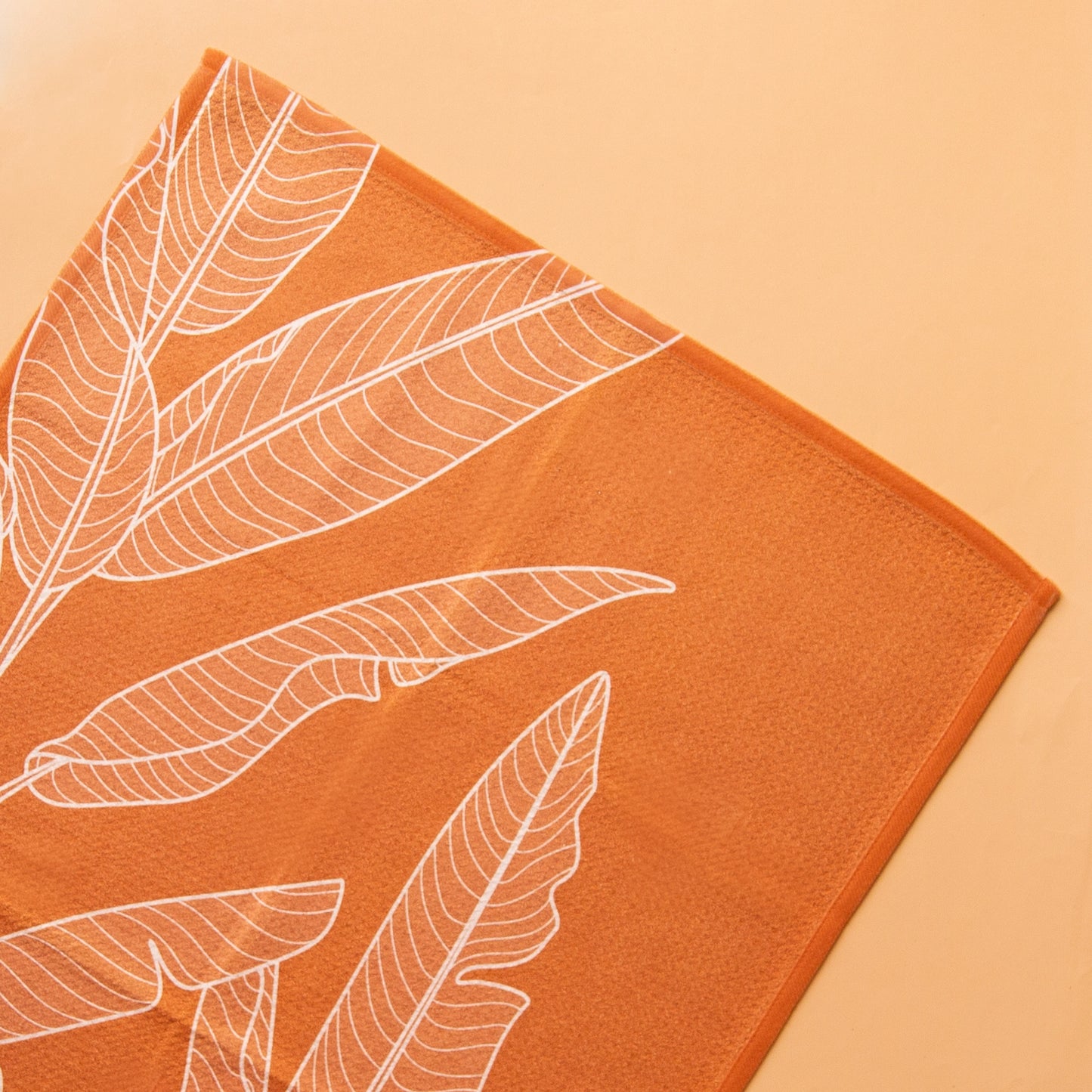 On an orange background is an orange kitchen towel with a white banana leaf design.