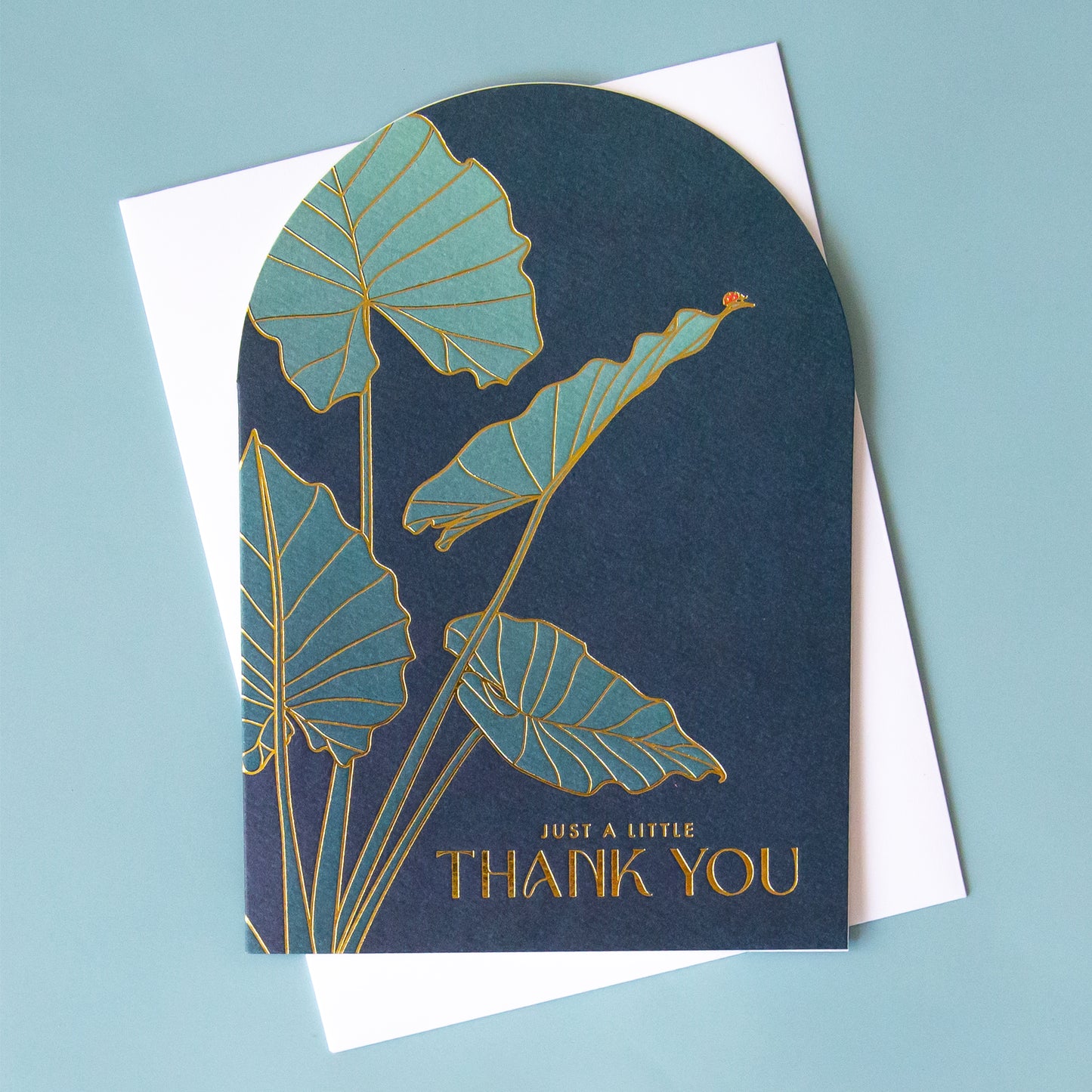 A blue arched shape card with a plant illustration on the front and gold foiled text that reads, "Just A Little Thank You".