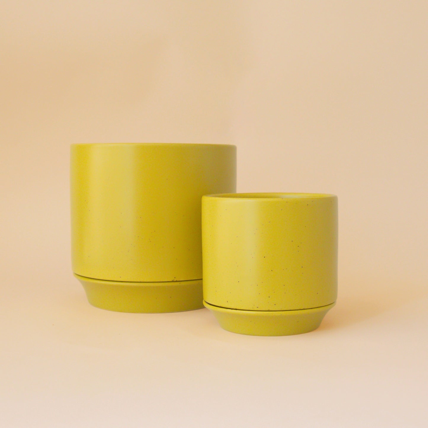 Two beautiful ceramic pots in a yellow-green color sit in middle of image with soft orange background.
