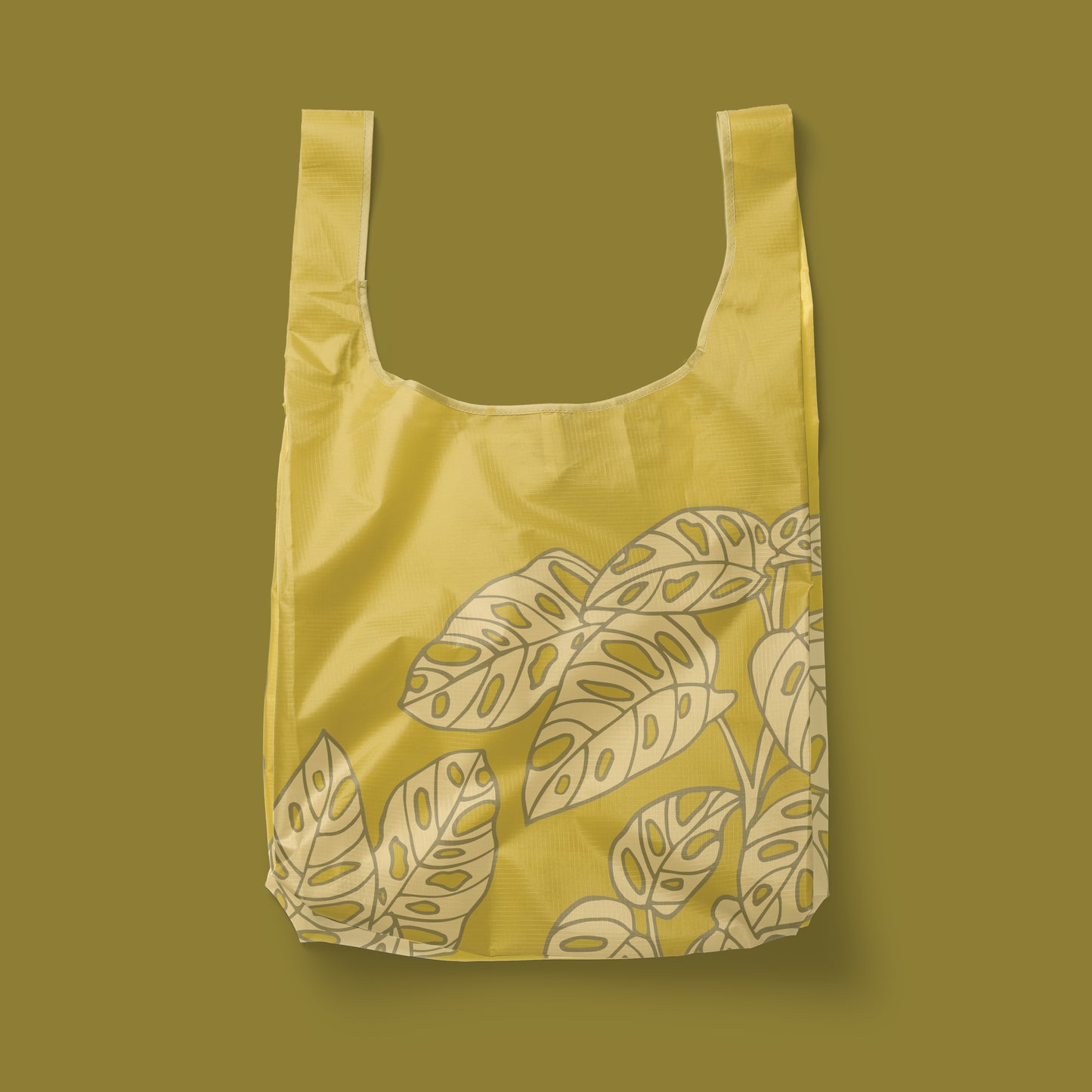 A green reusable nylon tote bag with a swiss cheese leaf pattern.