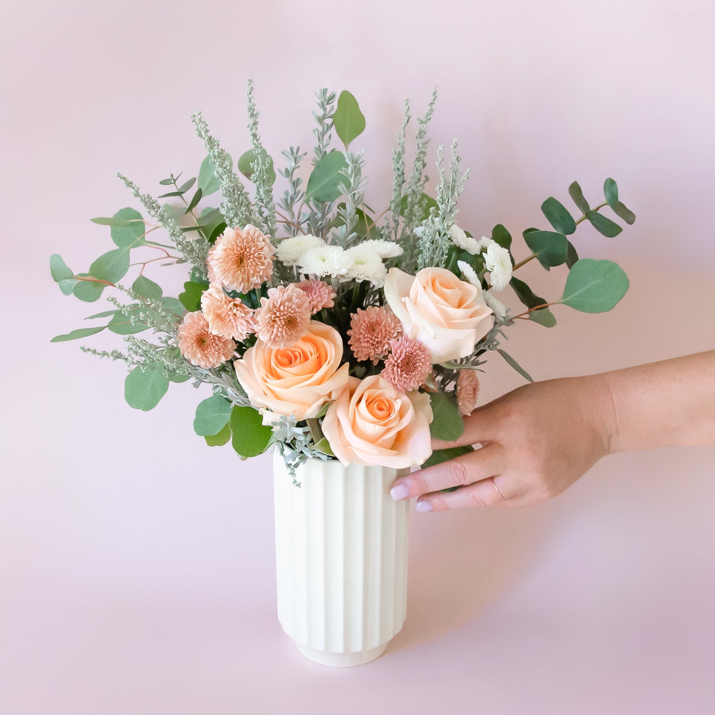 A white ribbed ceramic vase filled with a flower arrangement not included with purchase.