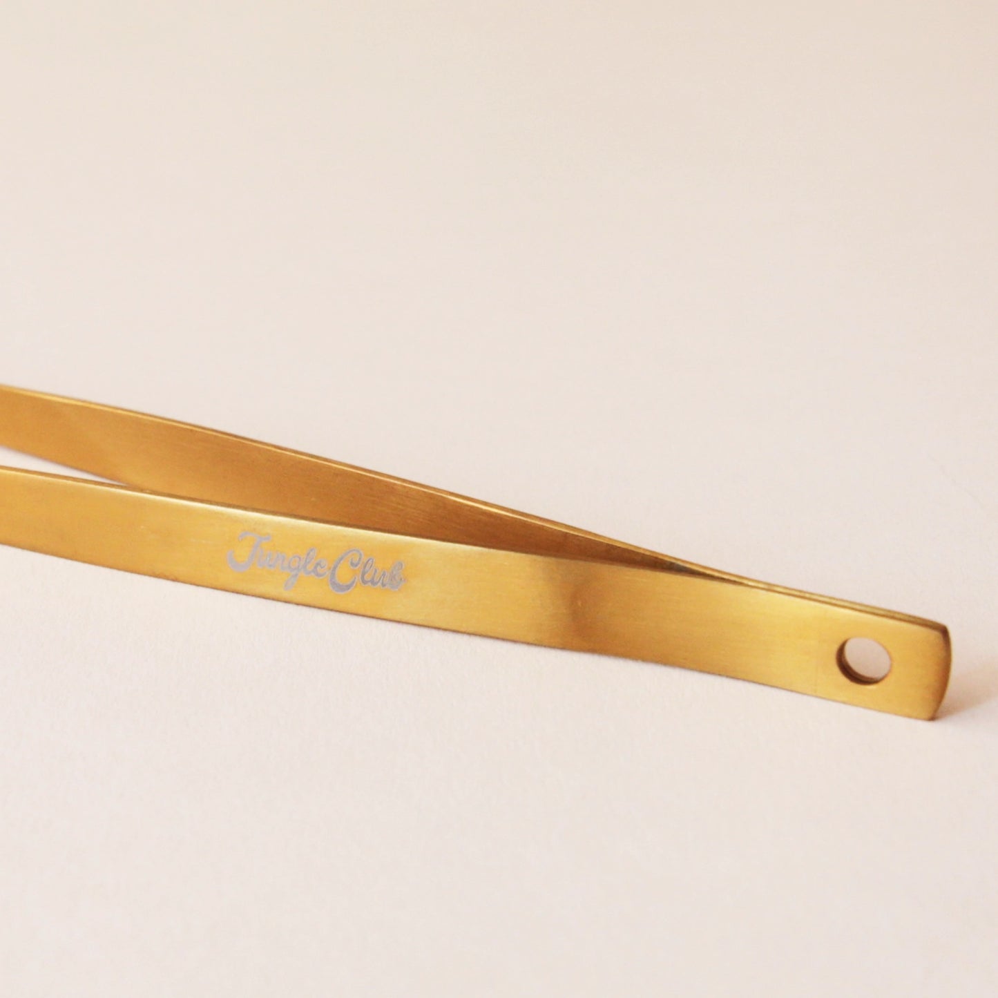 Brass tweezers with a slim design and a pointed tip perfect for handling spiky cacti. On the side of the tweezer there is text that reads, "Jungle Club" I white cursive.