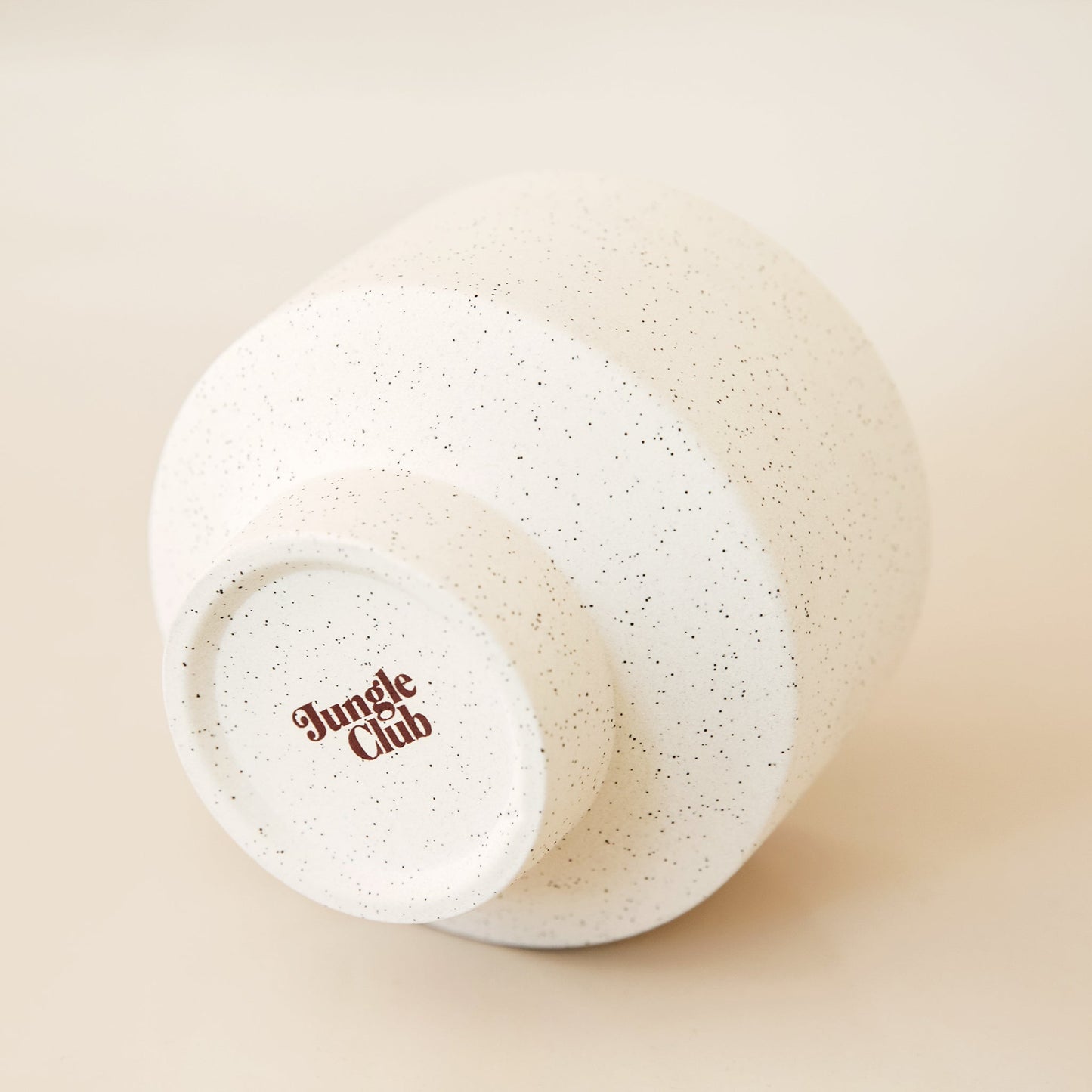 Bottom view of ivory speckled pot. The bottom of the pot reads 'jungle club' in a rust color.