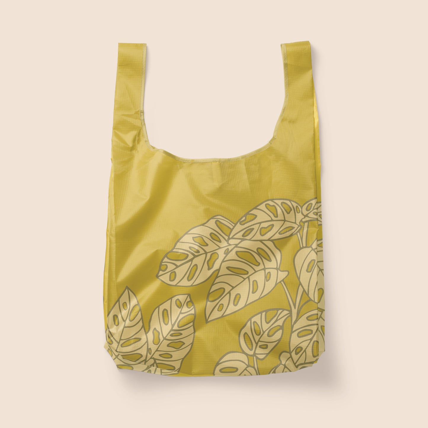 Photographed in front of a white background is a green nylon reusable bag with a lighter green Swiss cheese plant print on the front and back.