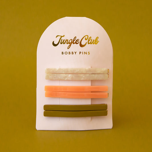 On a white packaging is six bobby pin clips in three different colors. From top to bottom is an ivory shell shade, mango orange, and olive green shade.