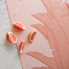 On a marble background is a light salmon colored kitchen towel with a waffle texture and a bird of paradise print. In this photograph, it is staged with a sliced blood orange.
