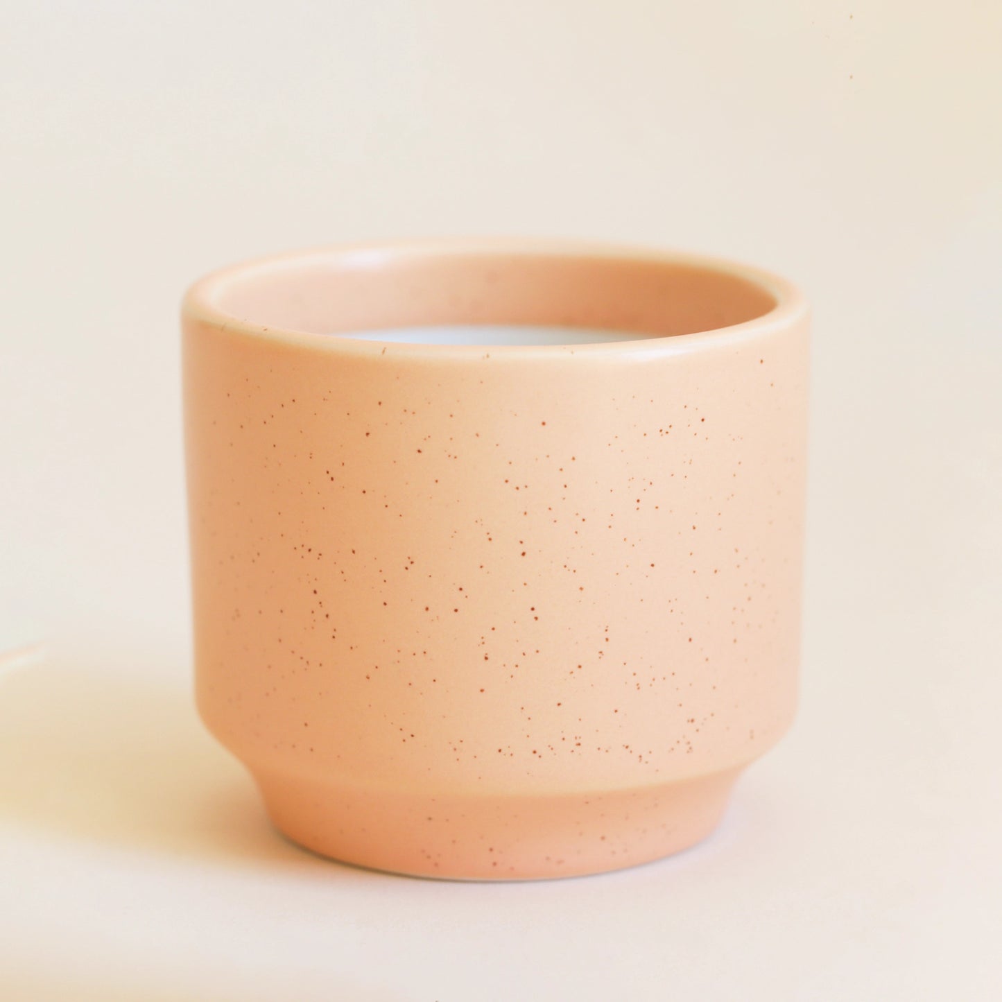 On an ivory background is a ceramic planter in a salmon, pinkish orange shade with a speckle detail and a tapered base.