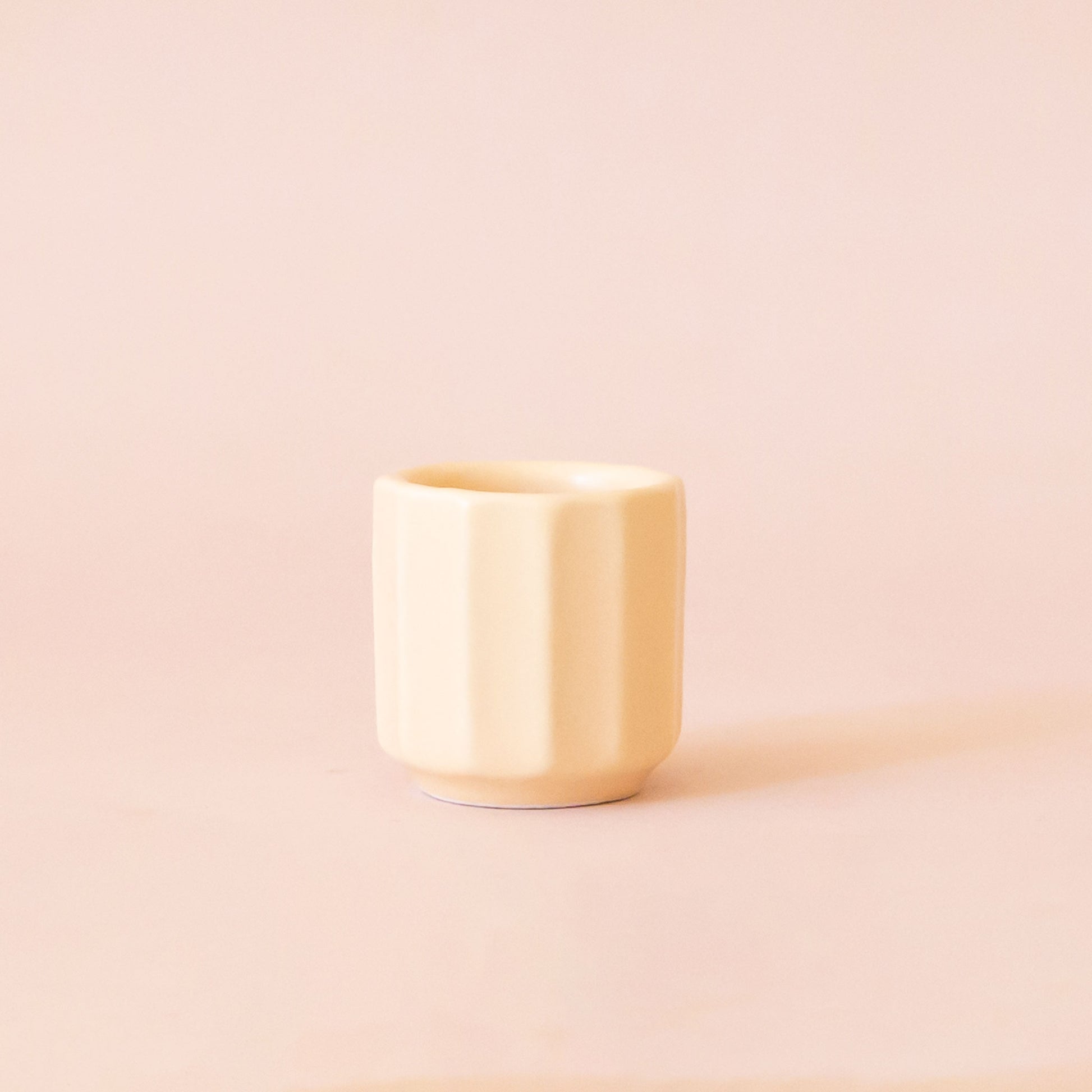 An itty bitty pot about the size of thimble that is a soft beige color sits in the middle of a page.  The background is all a soft white color.