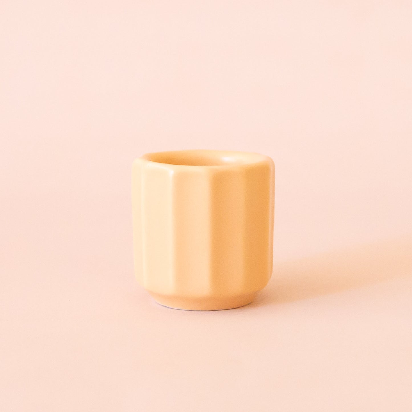 An itty bitty pot about the size of thimble that is a soft peach color sits in the middle of page.  The tiny pot has little ridges all around it.  The background is all  a soft white color.