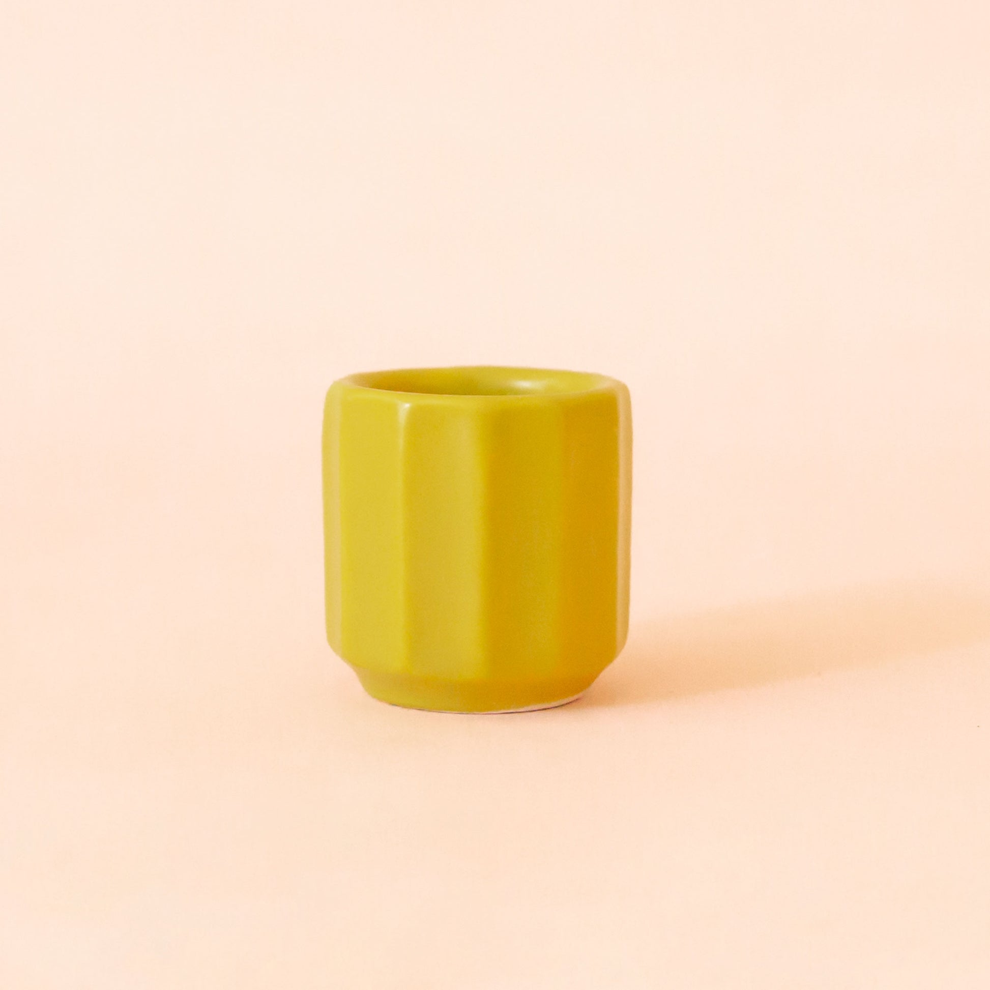 An itty bitty pot about the size of thimble that is a chartreuse color sits in the middle of the page.  The background is all  a soft white color.