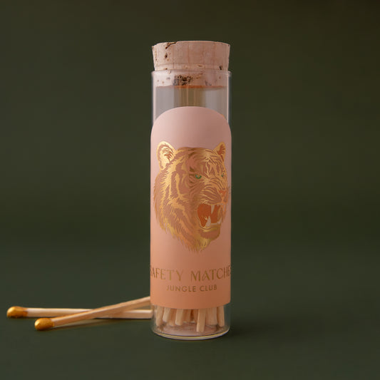 Clear glass vial with a cork lid that contains wooden safety matches. The label on the vial has a gold foil tiger on it. 