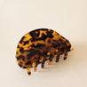 On a neutral background is a dark brown tortoise print claw clip with a round edge.