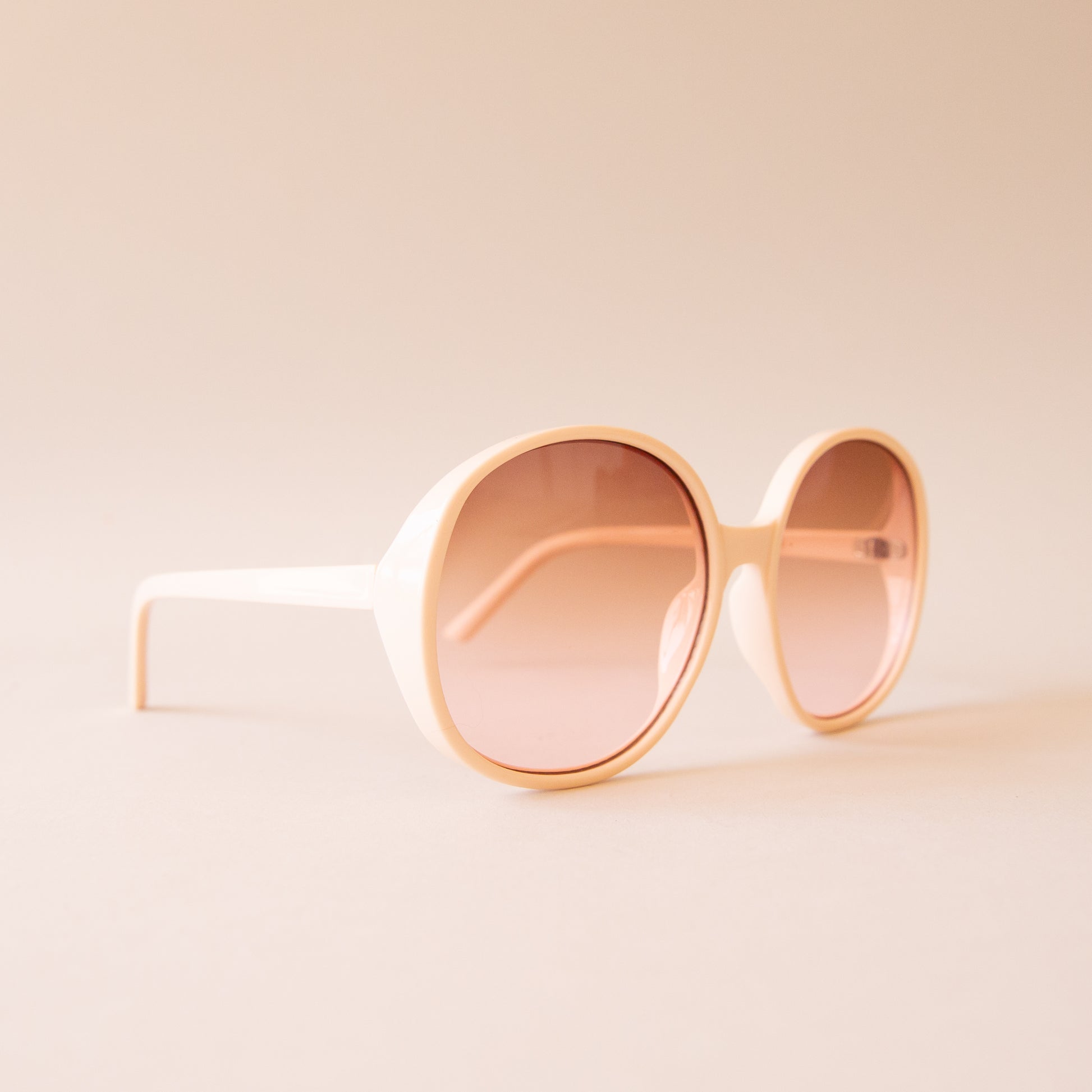 A creamy white pair of round oversized sunglasses with a light brown pinkish lens.