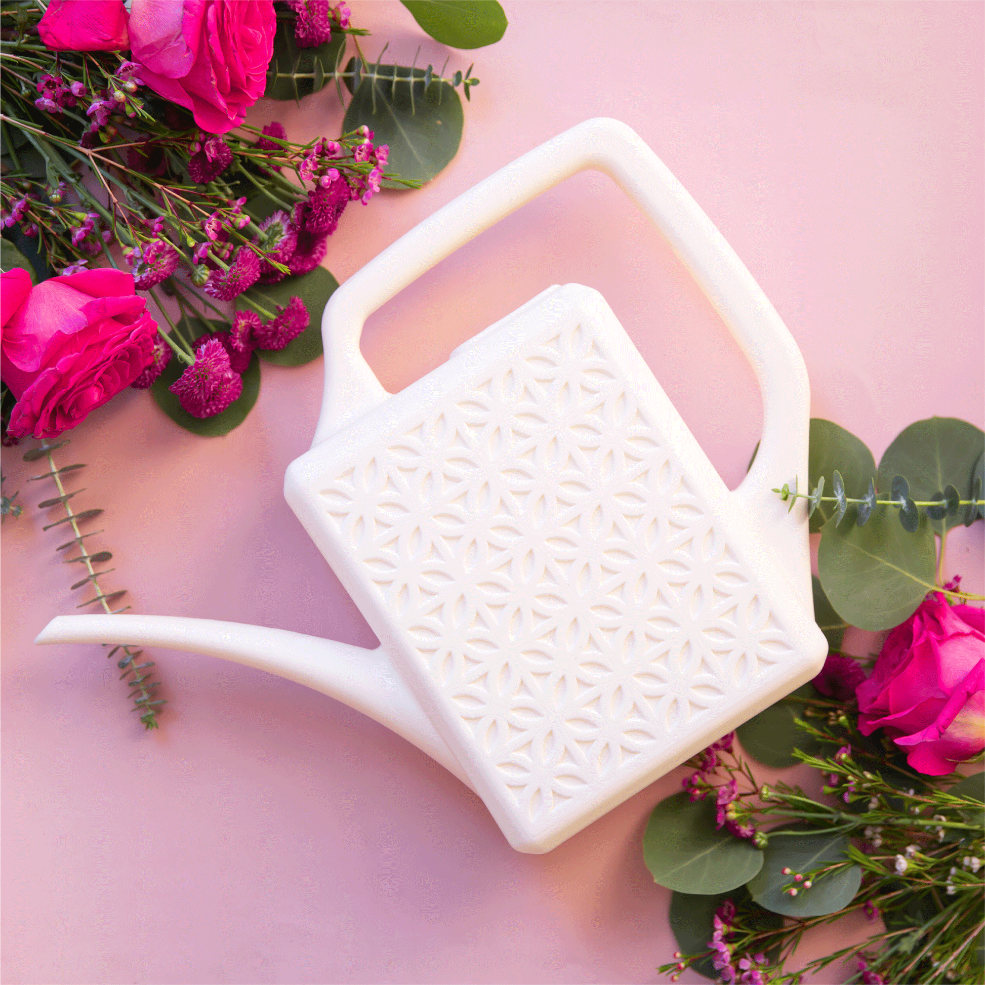 On a pink background is a white watering can with a long spout and a breeze block design on the side.