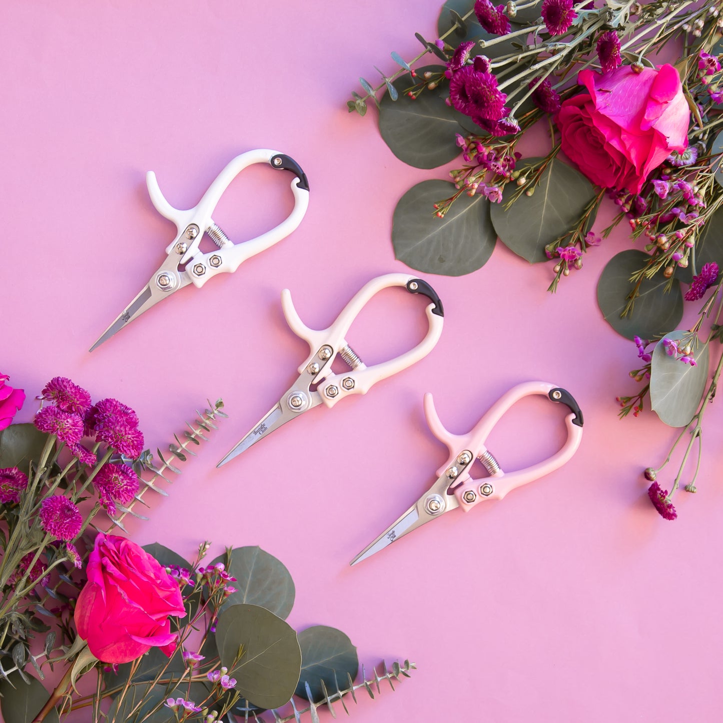 On a pink background is the three color ways of pruning shears next to bouquets of flowers.