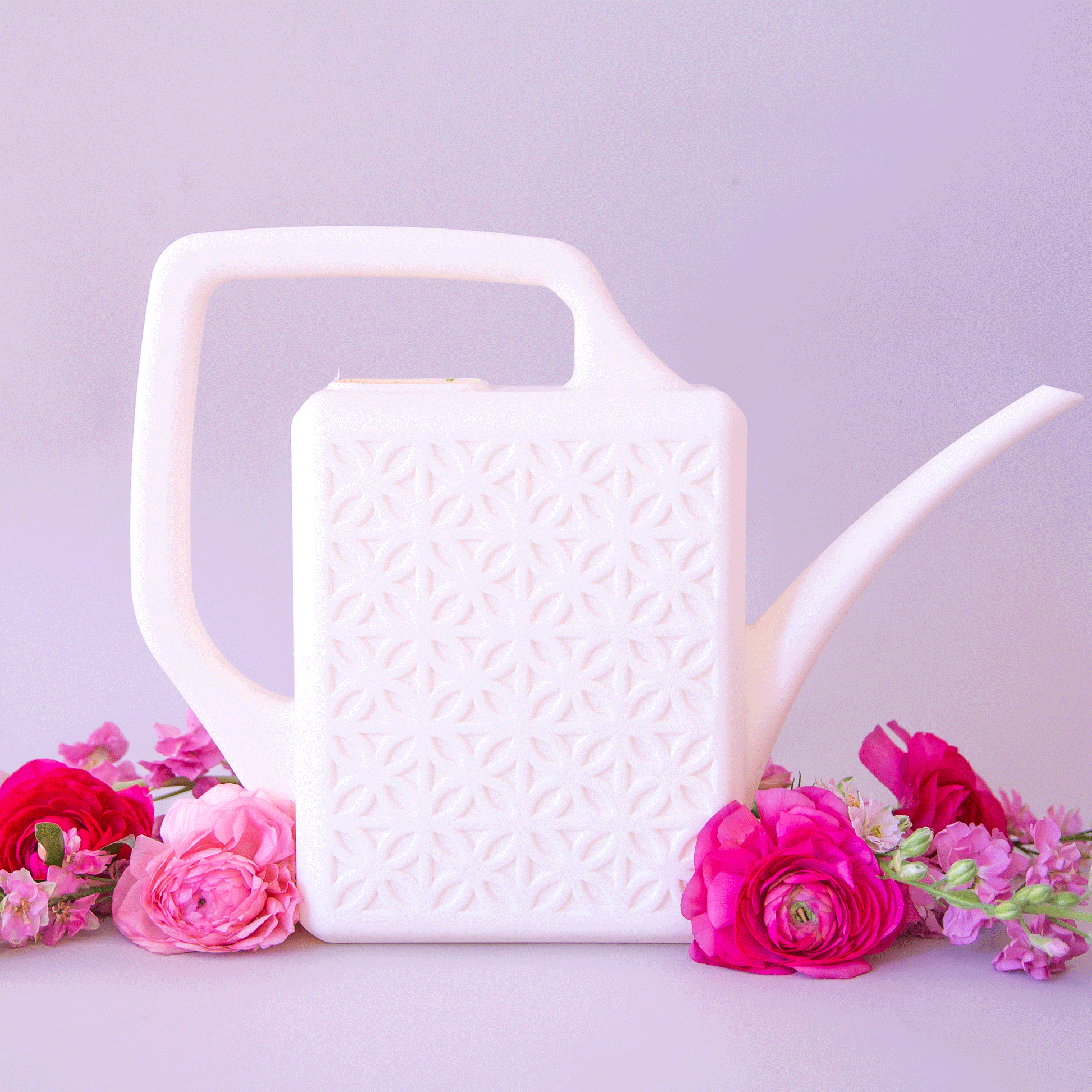 On a purple background is a white watering can with a long spout and a breeze block design on the side.