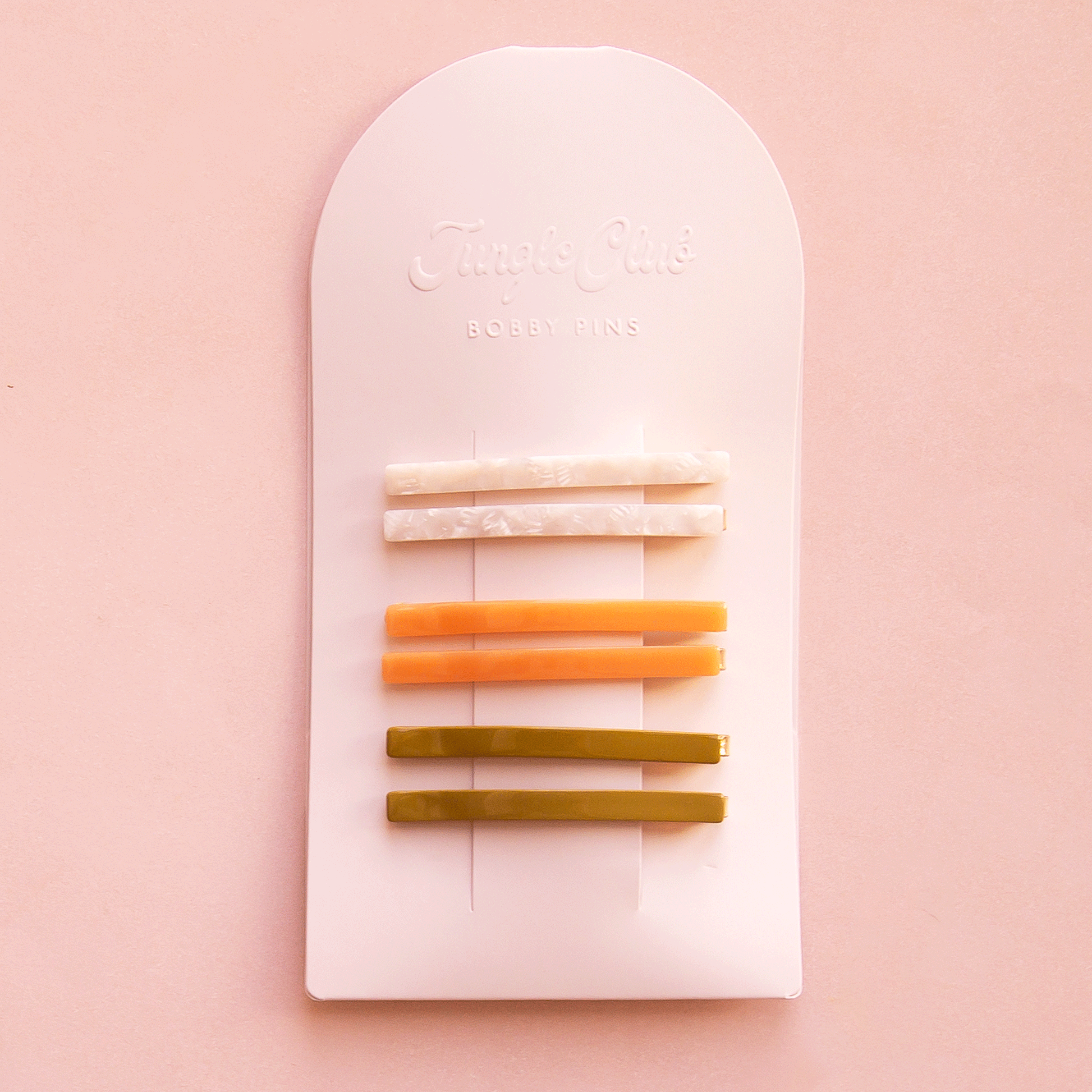 On a white packaging is six bobby pin clips in three different colors. From top to bottom is an ivory shell shade, mango orange, and olive green shade.