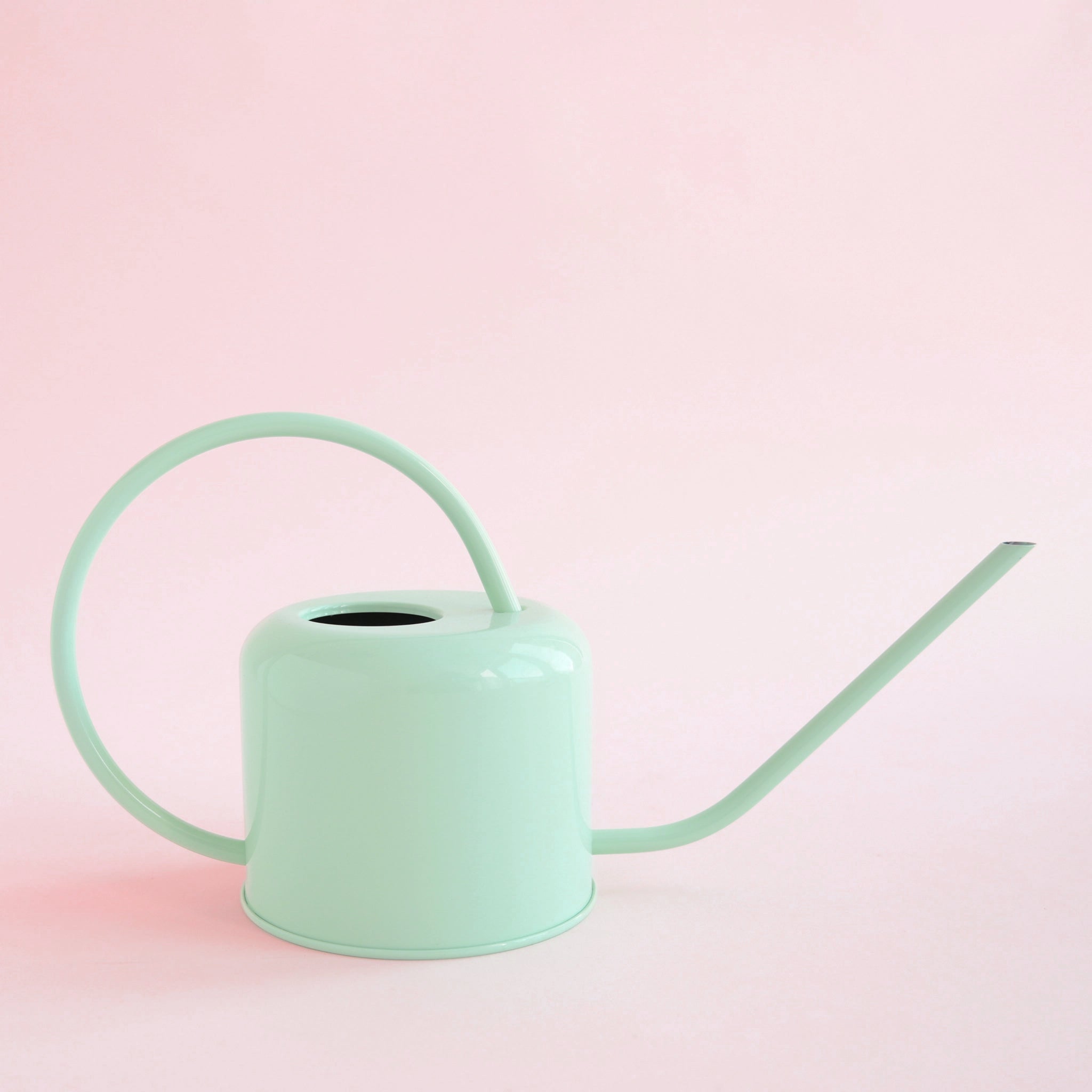 On a pink background is a light blue watering can with a long spout and a rounded handle.