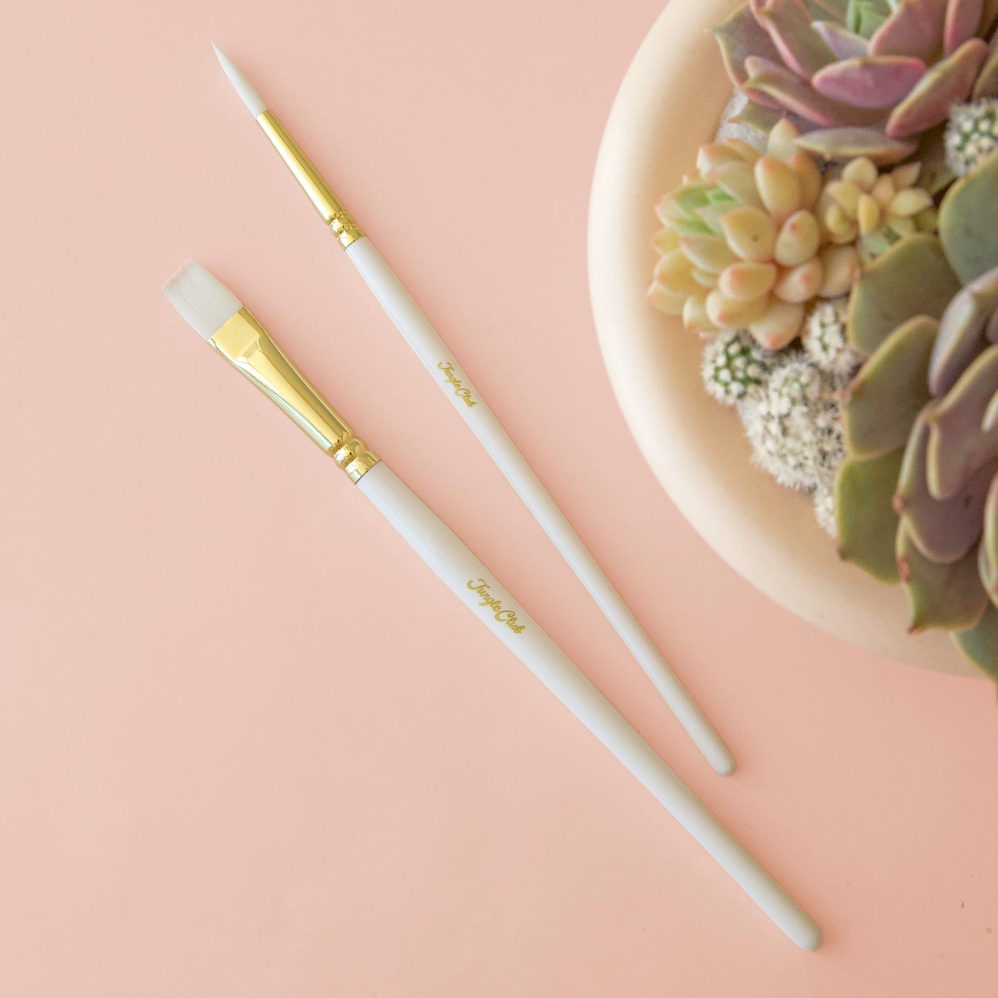 White and gold brushes laid flat against pink background