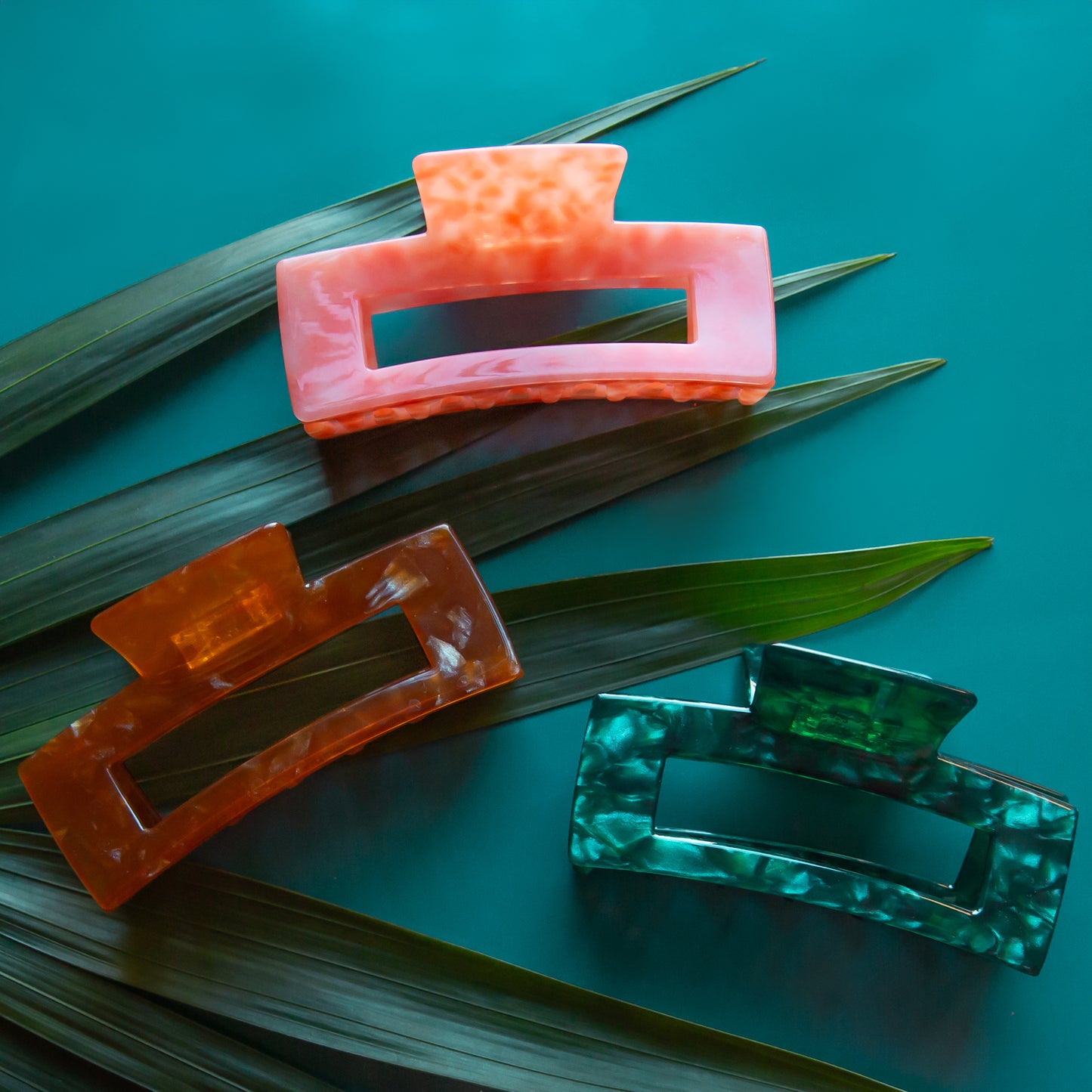 A set of three rectangle claw clips, one warm brown, one coral and one green. 