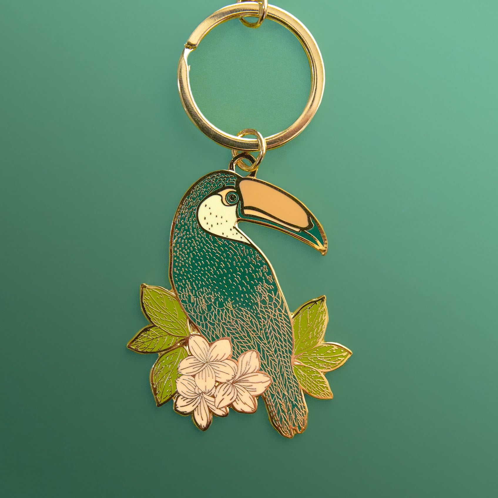 A gold enamel keychain shaped like a toucan on a blue ground.
