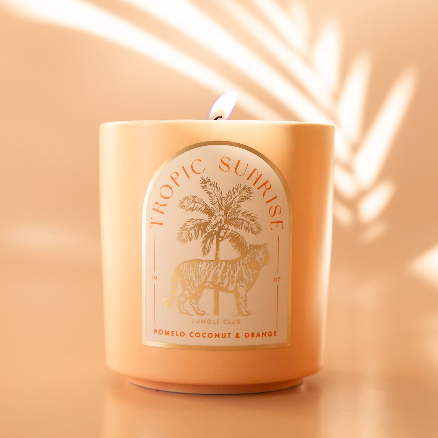 A light peach colored candle with a tiger and palm tree graphic and text above that reads, 'Tropic Sunrise'. 