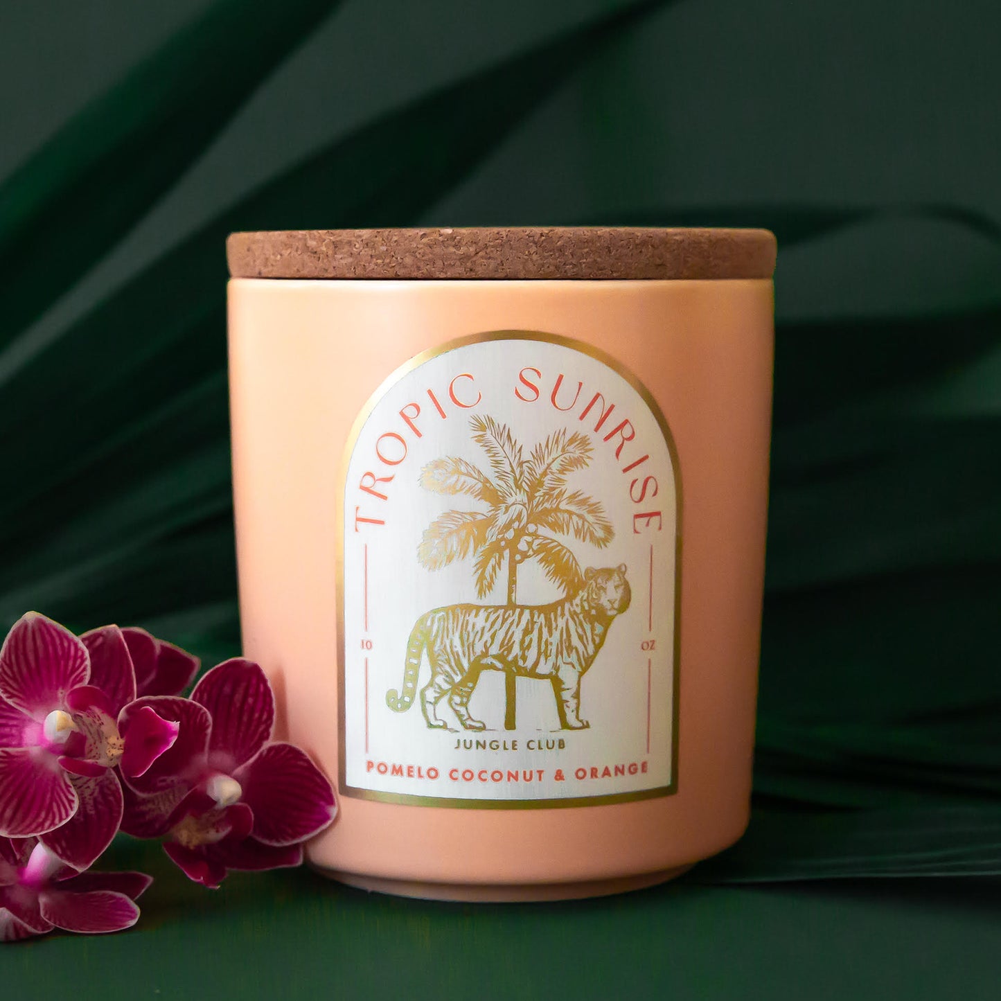 A light peach colored candle with a tiger and palm tree graphic and text above that reads, 'Tropic Sunrise'. 