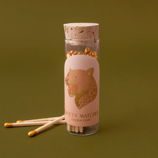 Clear glass vial with a cork lid that contains wooden safety matches. The label on the vial has a gold foil leopard on it. 