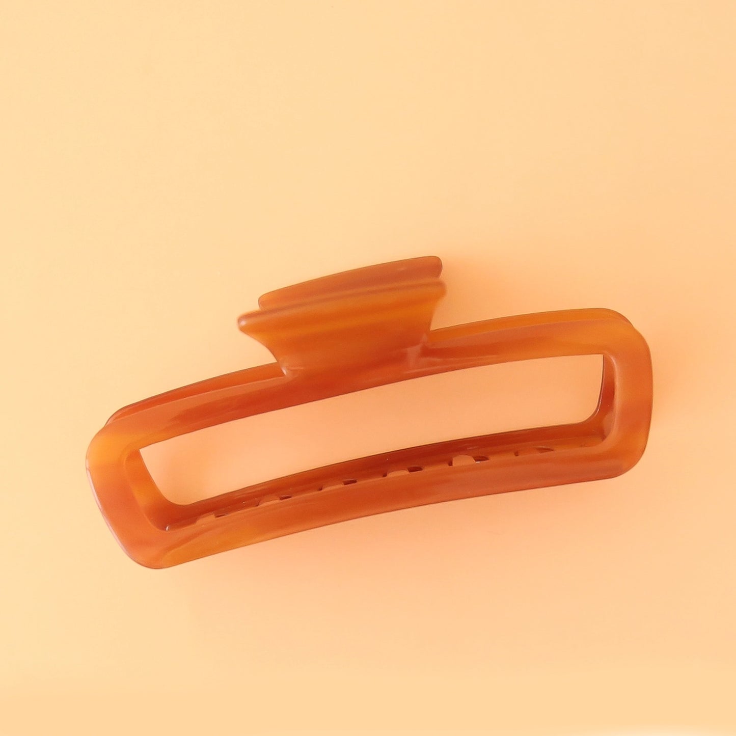On a peachy background is the Cabana Claw Clip in the shade Honey which is an orangey, amber shade.