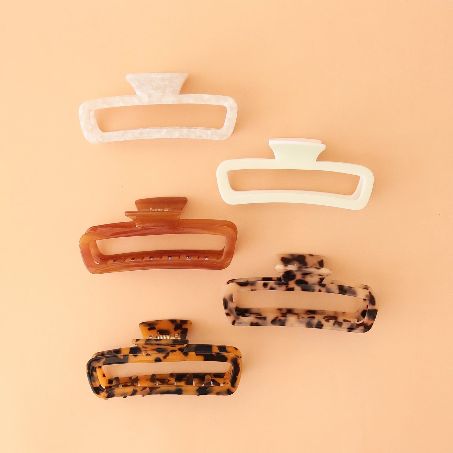 On a peachy background is the five available color options for the Cabana Hair Claw. It comes in a dark tortoise, light tortoise, amber, ivory and an ivory shell pattern.