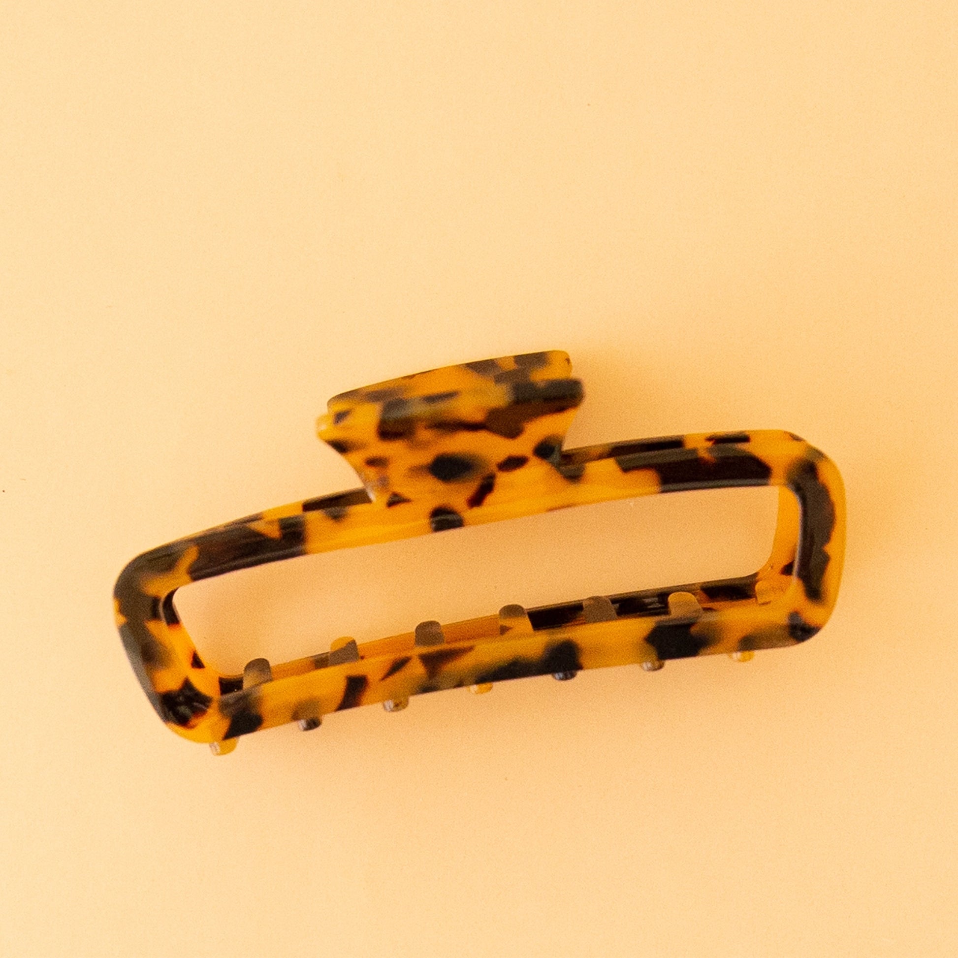 On a peachy background is a rounded rectangular shaped hair claw clip in the shade tortoise.