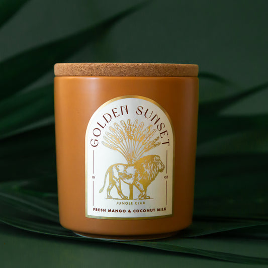 An orange candle with an arched label with a lion graphic and text above that reads, 'Golden Sunset'. 