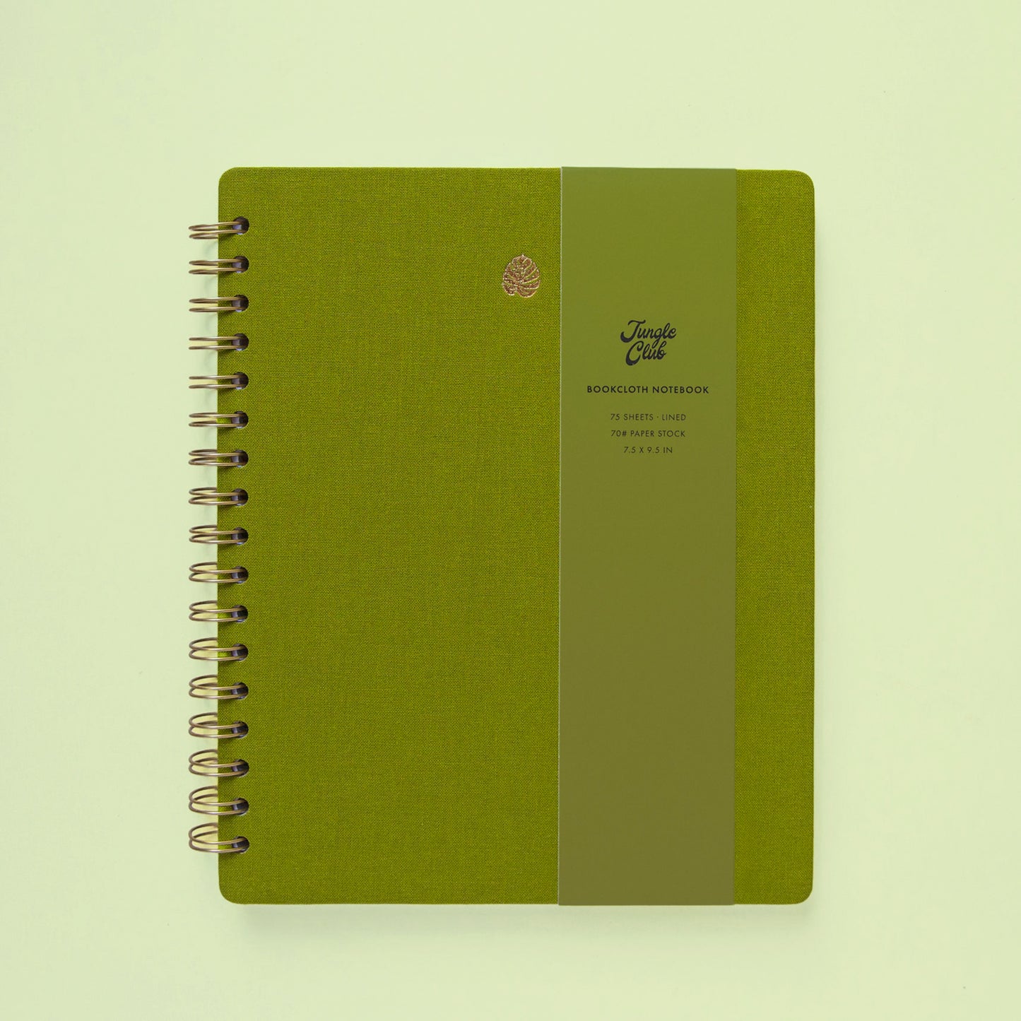 A green journal with a gold monstera leaf printed on it sits on a green background and leaves