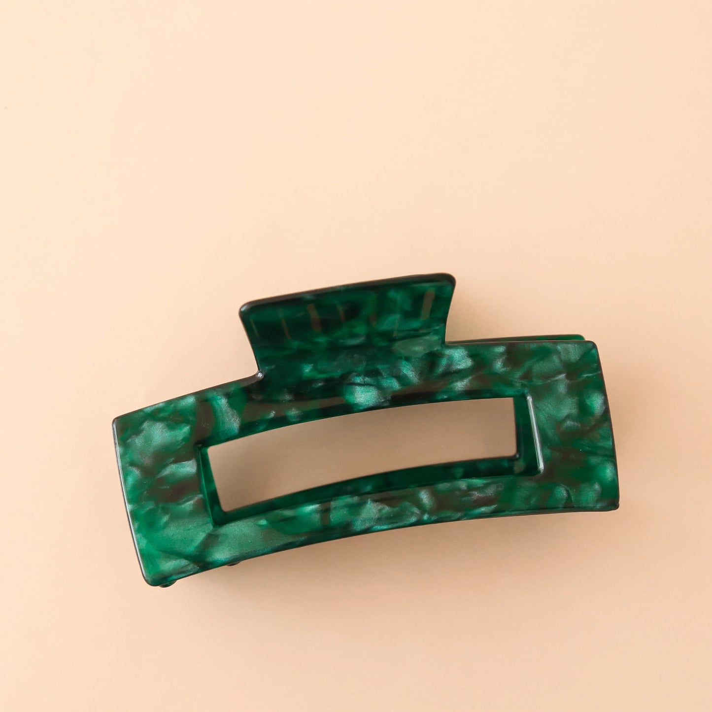 On a peachy background is a rectangular shaped claw clip in an emerald green shell like texture and shade.