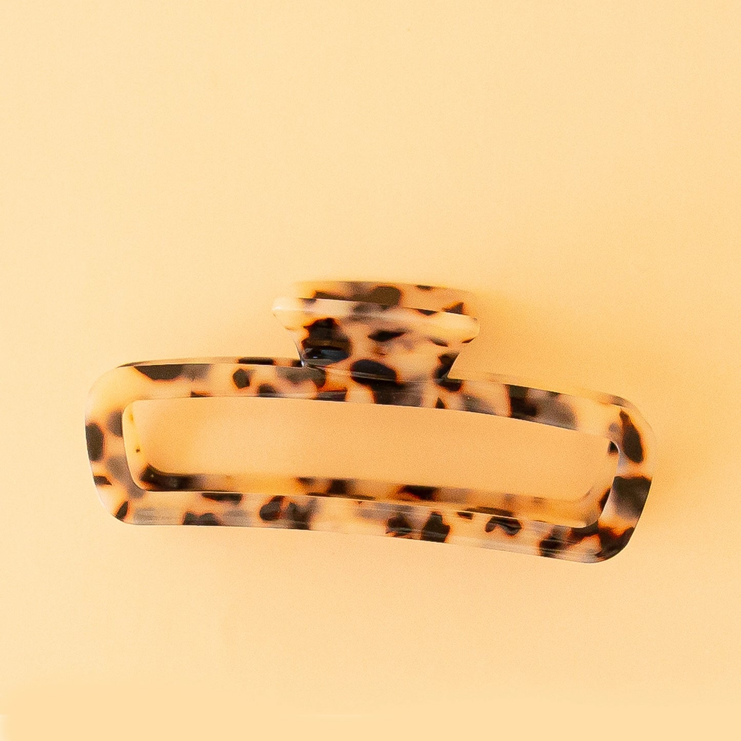 On a peachy background is a rounded rectangular shaped hair claw clip in the shade light tortoise