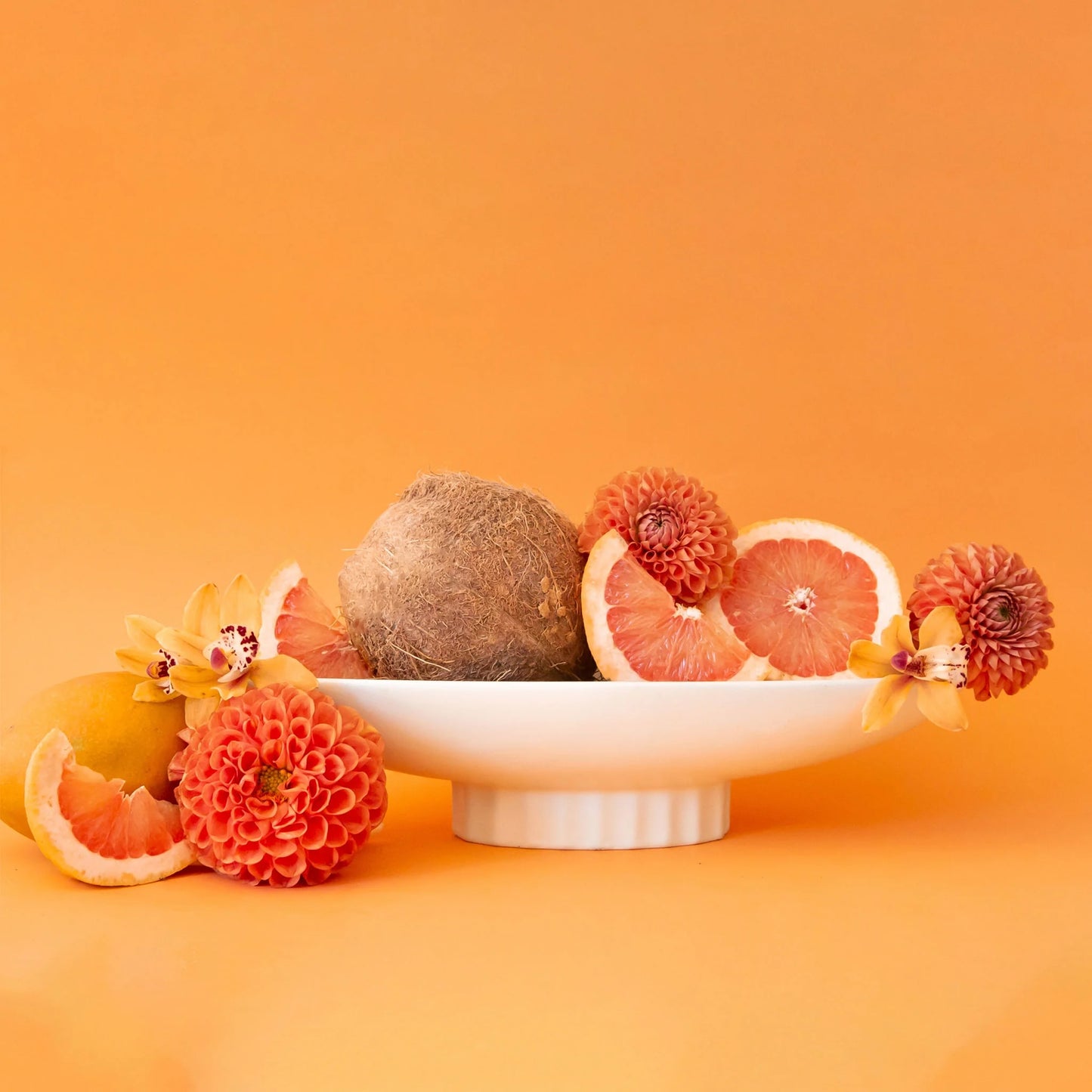 An elongated ceramic pedestal bowl filled with fruit and flowers. 