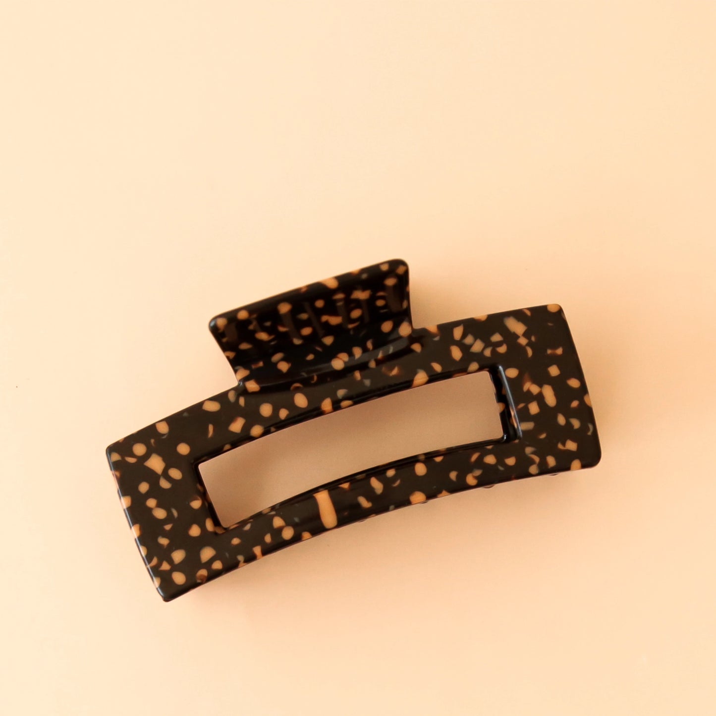 On a peach backgrounds a brown and orange spotted rectangular claw clip.