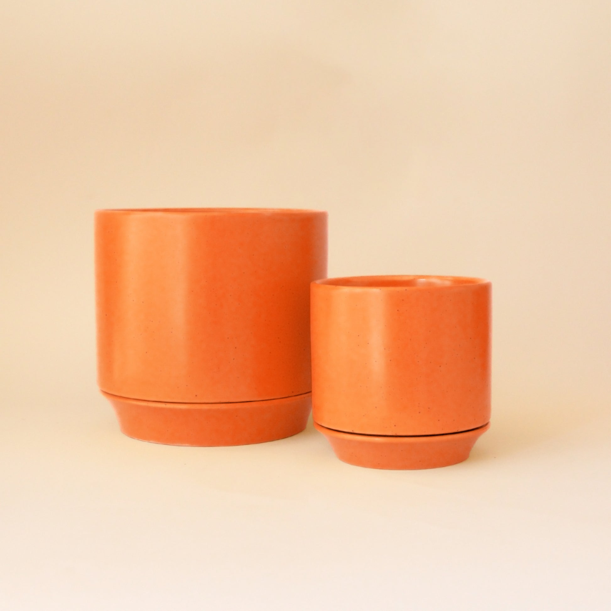 Two orange pots in small and medium size on a peach background.
