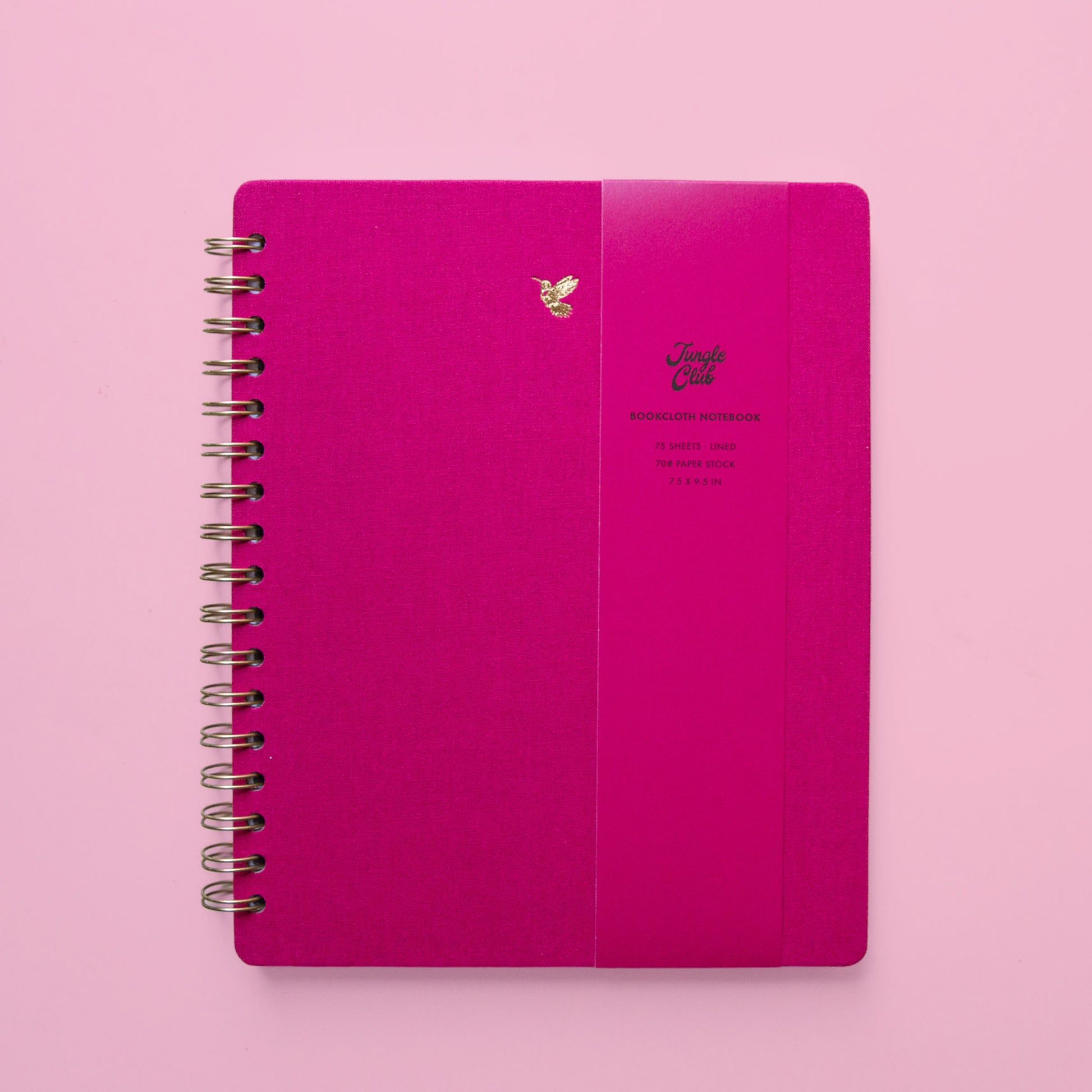 A hot pink spiral bound notebook with a gold foiled hummingbird graphic in the top center. 