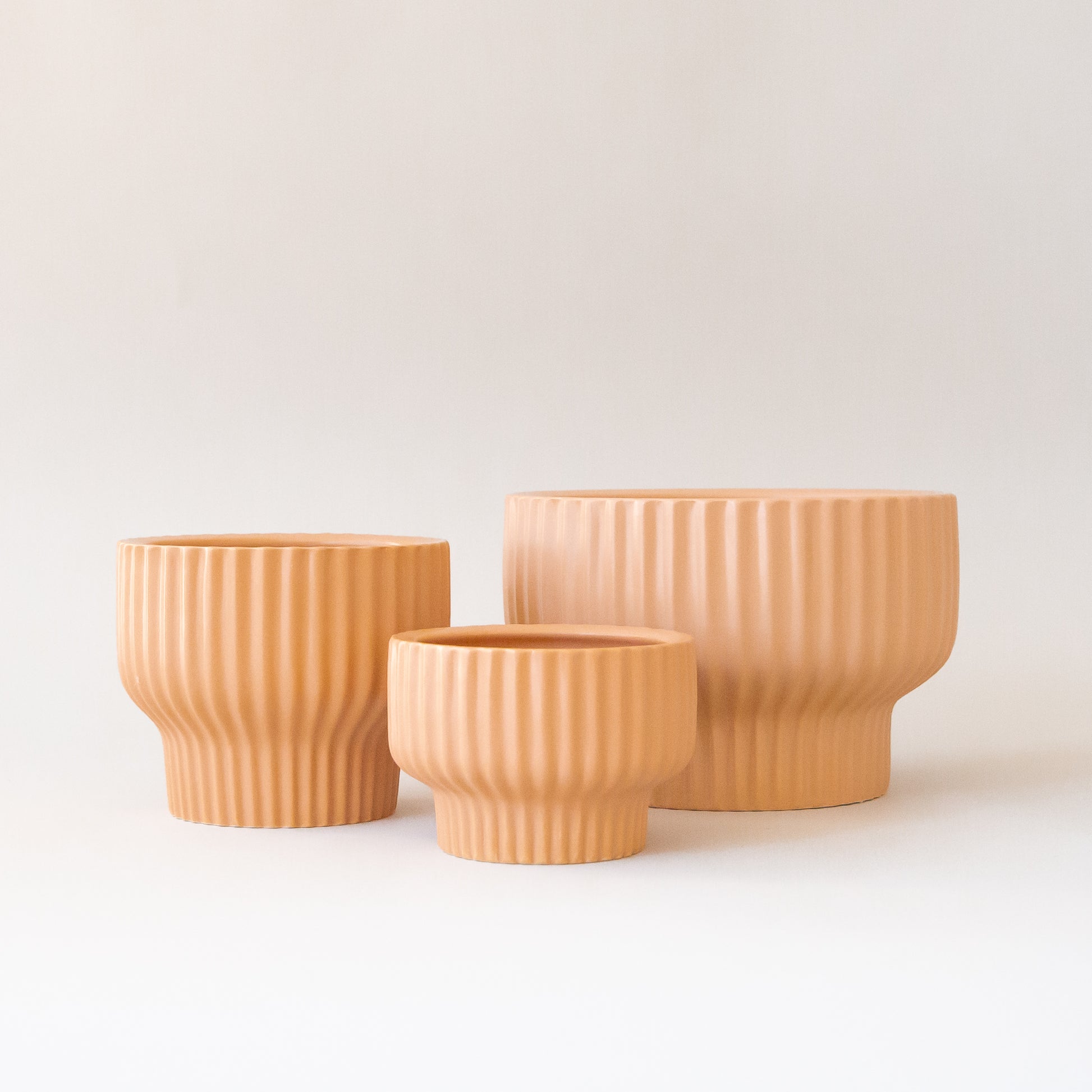 Three different sized tan / light orange ceramic pedestal planters with a ribbed texture. 