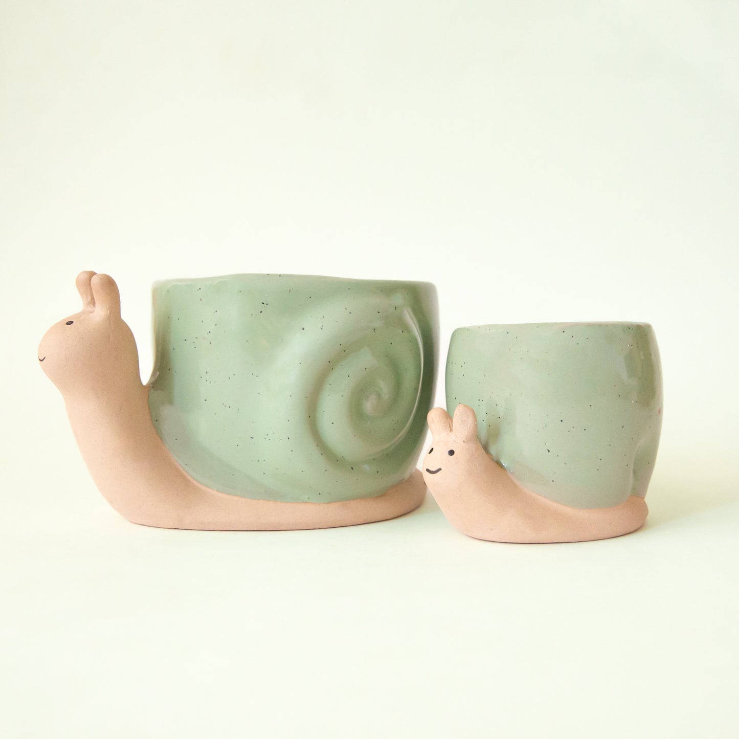 a pair of ceramic snail shaped planters with green shells and smiling expressions. 