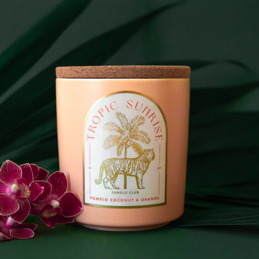 A light peach colored candle with a tiger and palm tree graphic and text above that reads, 'Tropic Sunrise'. 