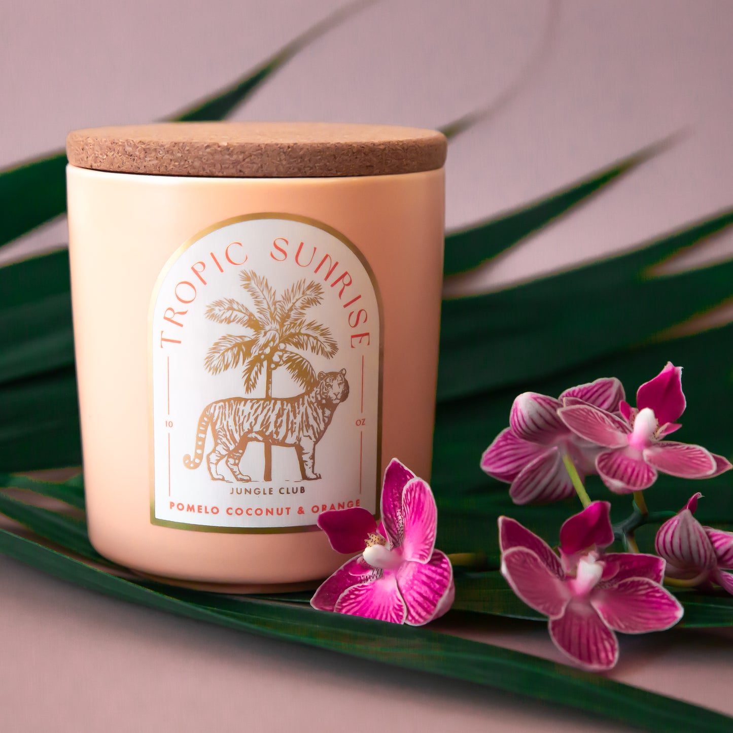 A light peach colored candle with a tiger and palm tree graphic and text above that reads, 'Tropic Sunrise'. 