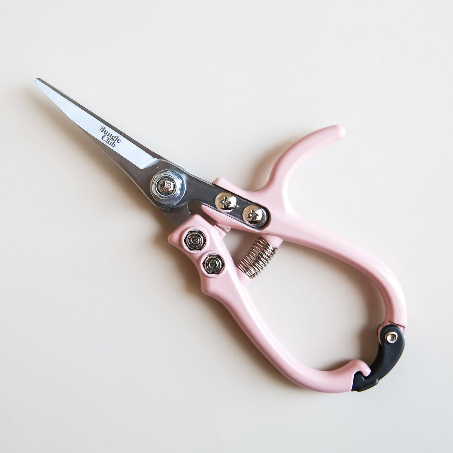 Pair of pruning shears with pastel pink handles and metal blades. The outer blade reads 'jungle club' in small, playful lettering. The pruning shears have a black clasp at the top of the handles to secure them closed.